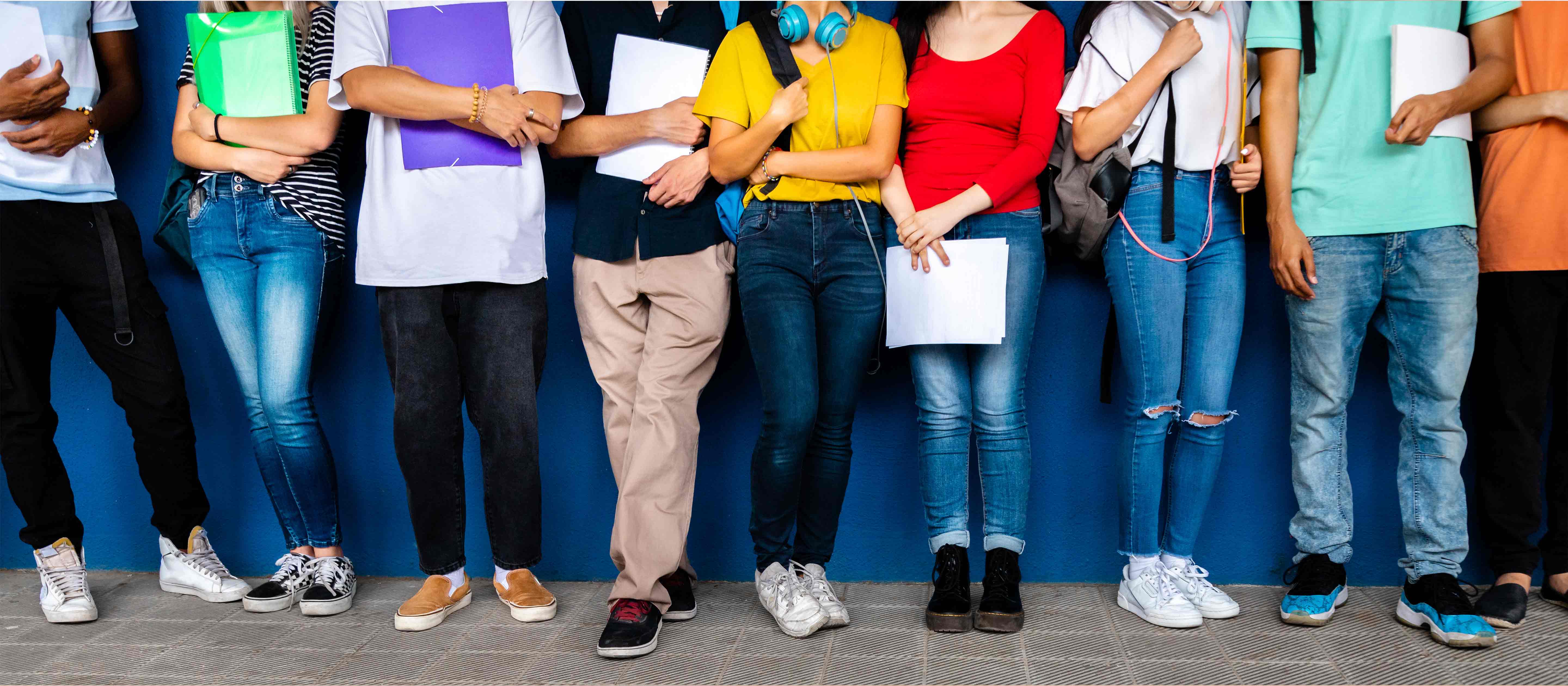 Group of high school teenagers standing against blue background wall.