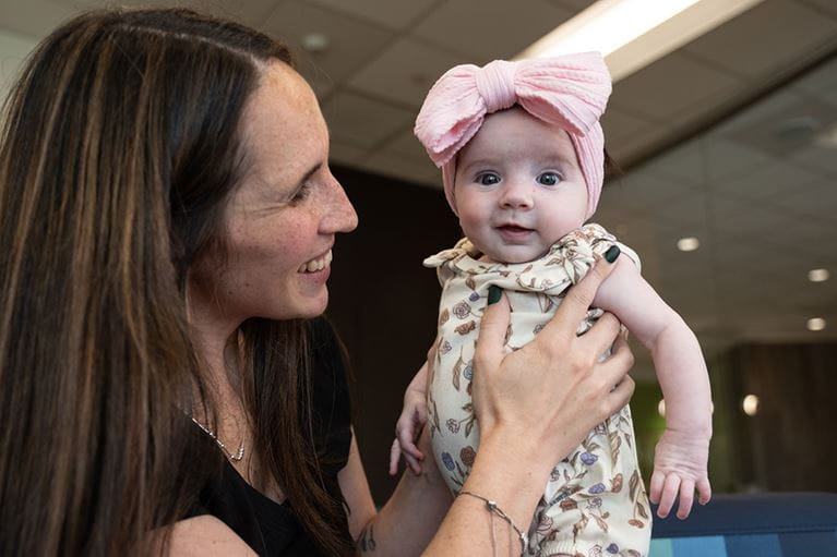 Woman holding infant girl with big, pink bow.