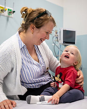 Mom smiling at happy child in hospital bed.