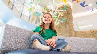 Smiling girl sitting cross-legged in the lobby of Champions Pavilion.